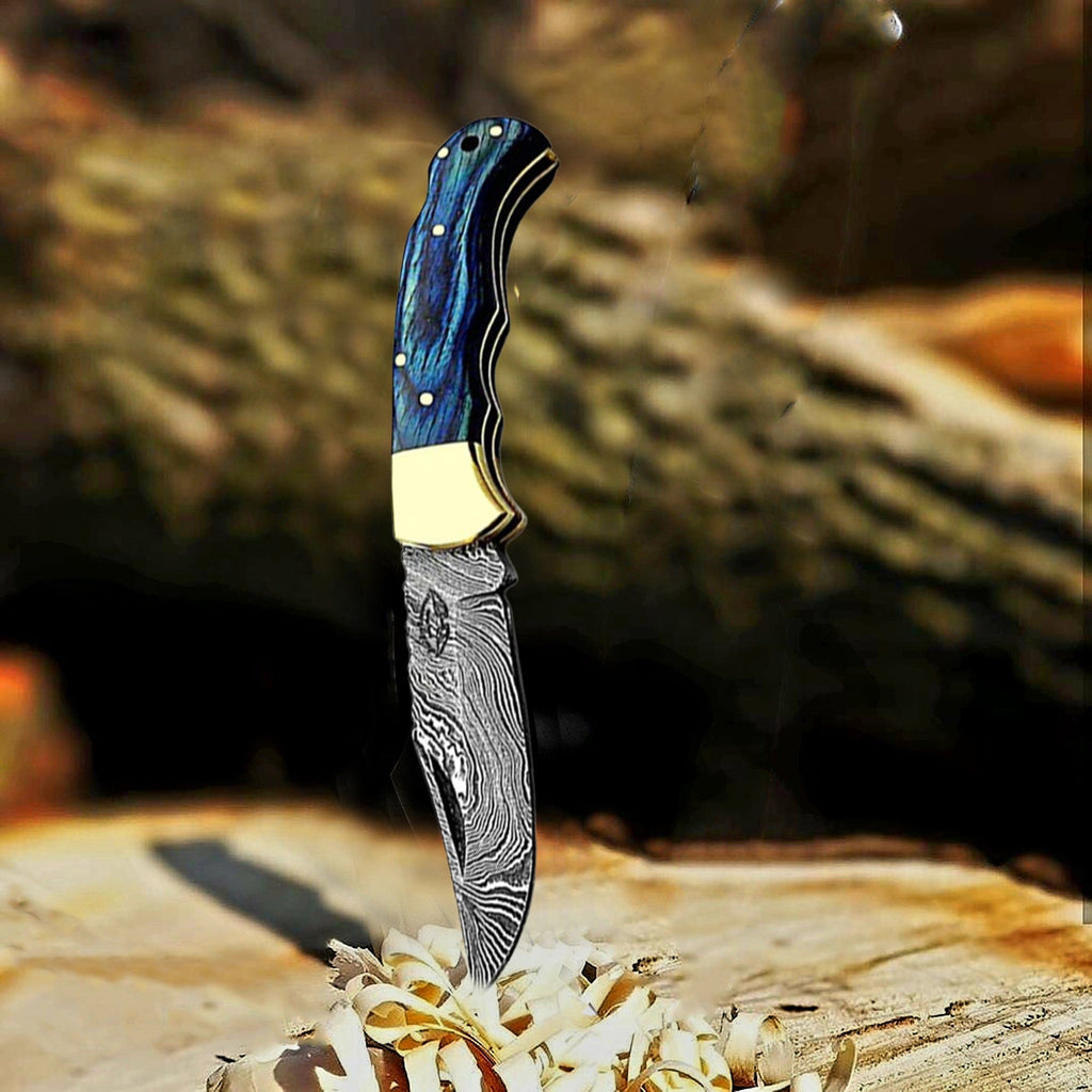 Blue wood handle Damascus folding pocket knife with brass bolster in a tree stump